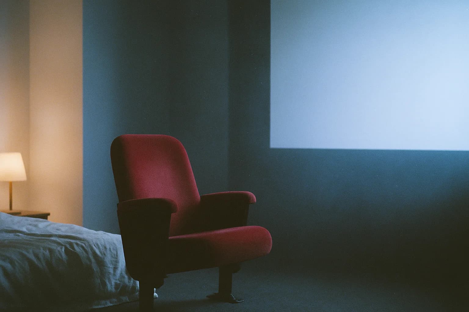Un siège de cinéma rouge vide face à un écran pâle dans une salle sombre, métaphore de l'observation des pensées le soir