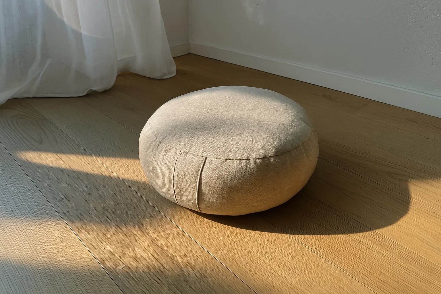 Coussin de méditation rond posé sur un parquet clair, ombre en diagonale projetée par une fenêtre