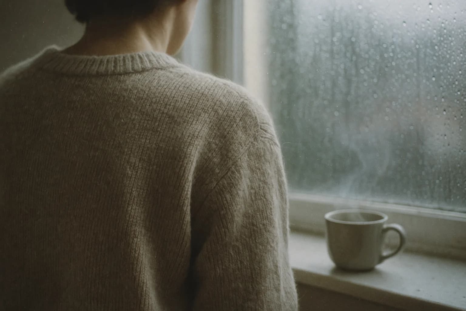 Une personne de dos près d'une fenêtre pluvieuse, image de pourquoi je manque de patience quand le corps est fatigué