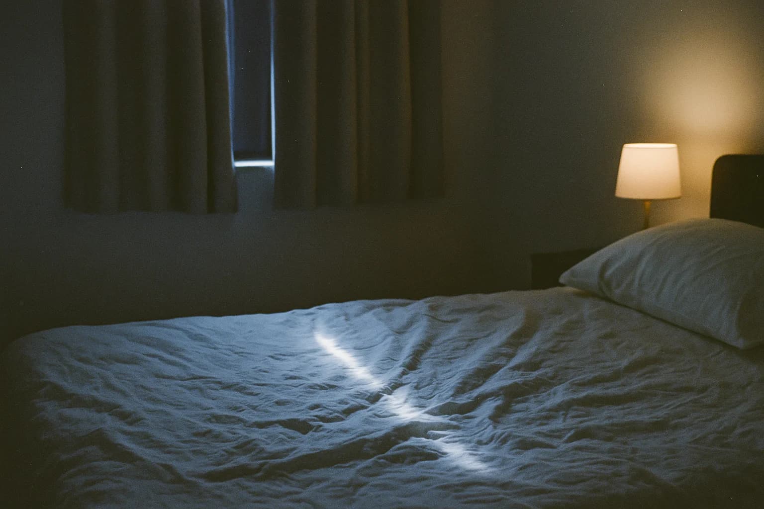 Se rendormir après un réveil nocturne : un drap froissé et un oreiller dans une chambre sombre, un filet de lumière entre les rideaux