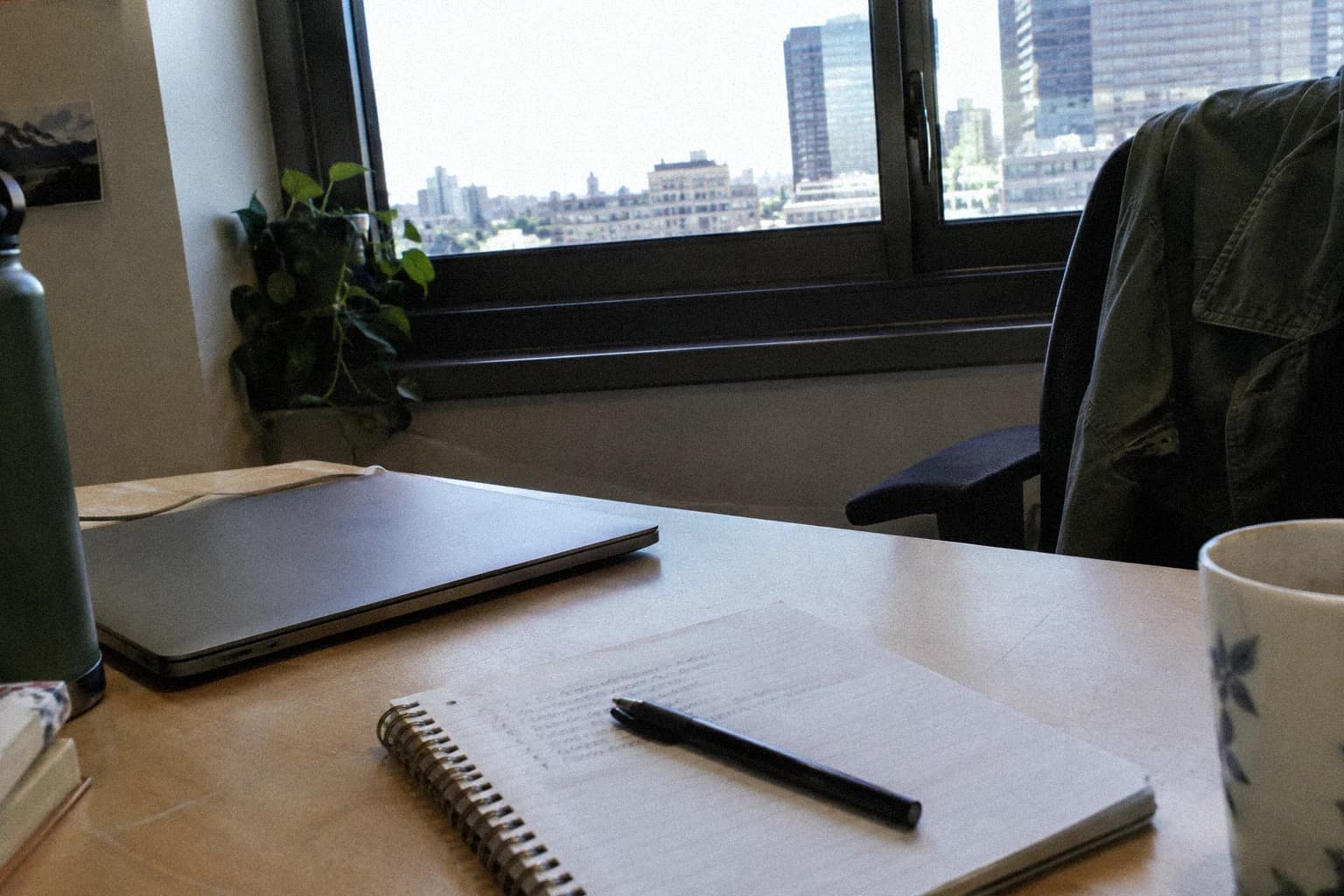 A desk at the end of the workday: an open spiral notebook with a few handwritten lines and a pen laid across the page, in front of a closed laptop