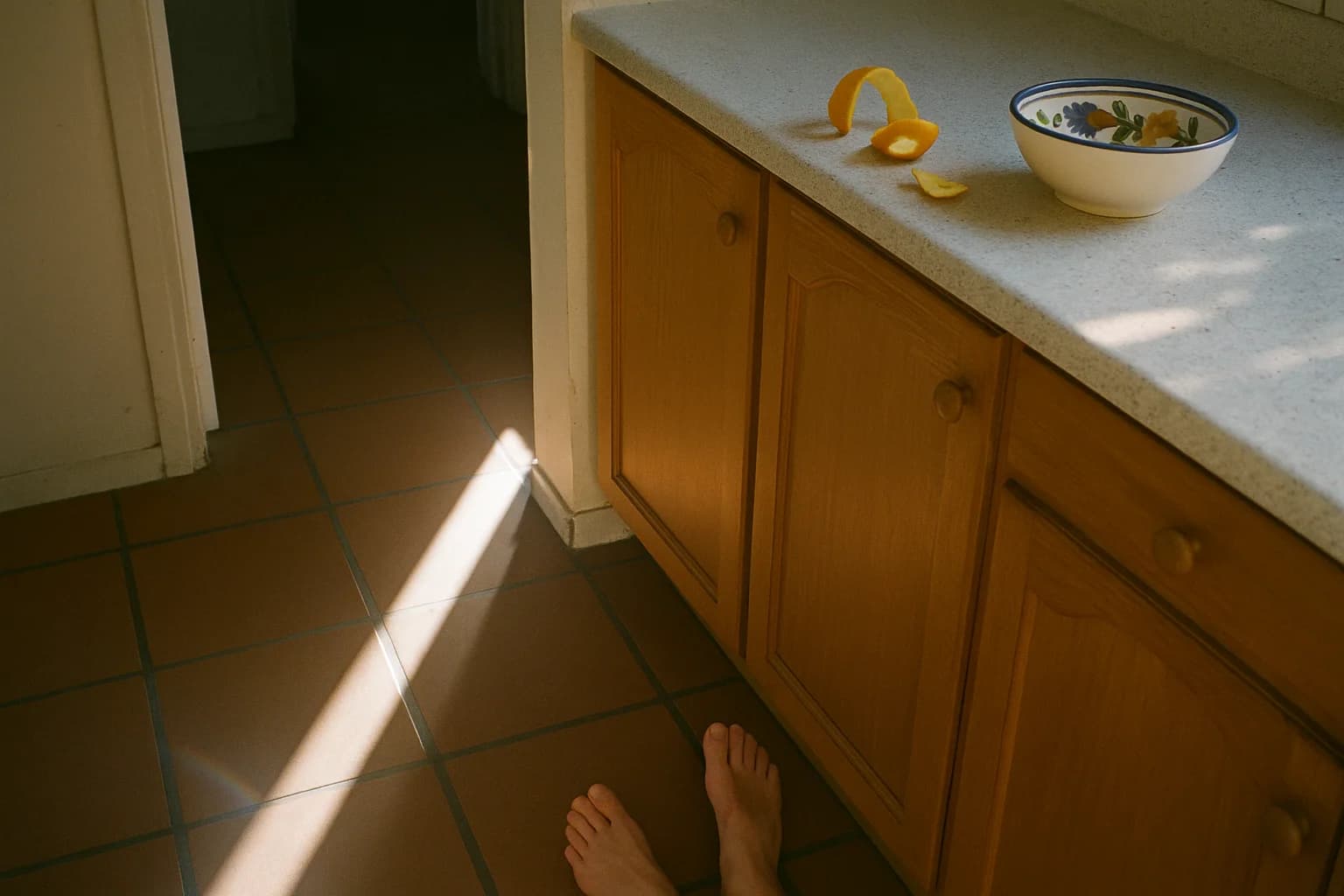 Bare feet on warm terracotta floor tiles, a strip of sunlight crossing a kitchen floor