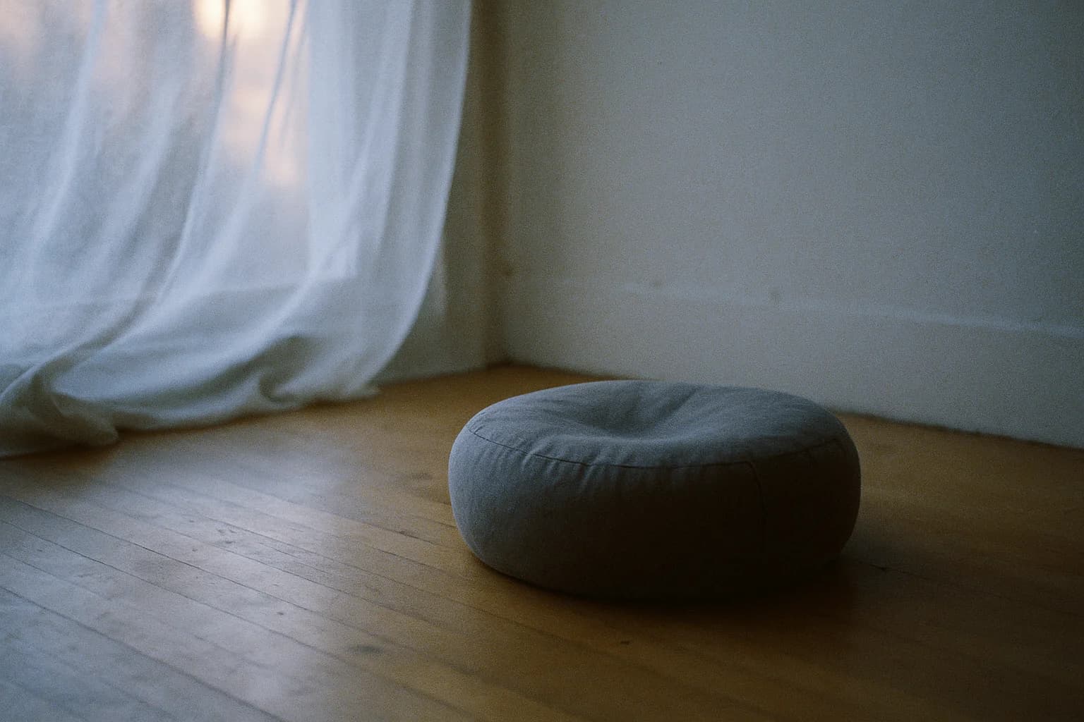 Coussin de méditation rond gris posé sur un parquet clair, léger creux au centre laissé par un poids, lumière douce de fenêtre