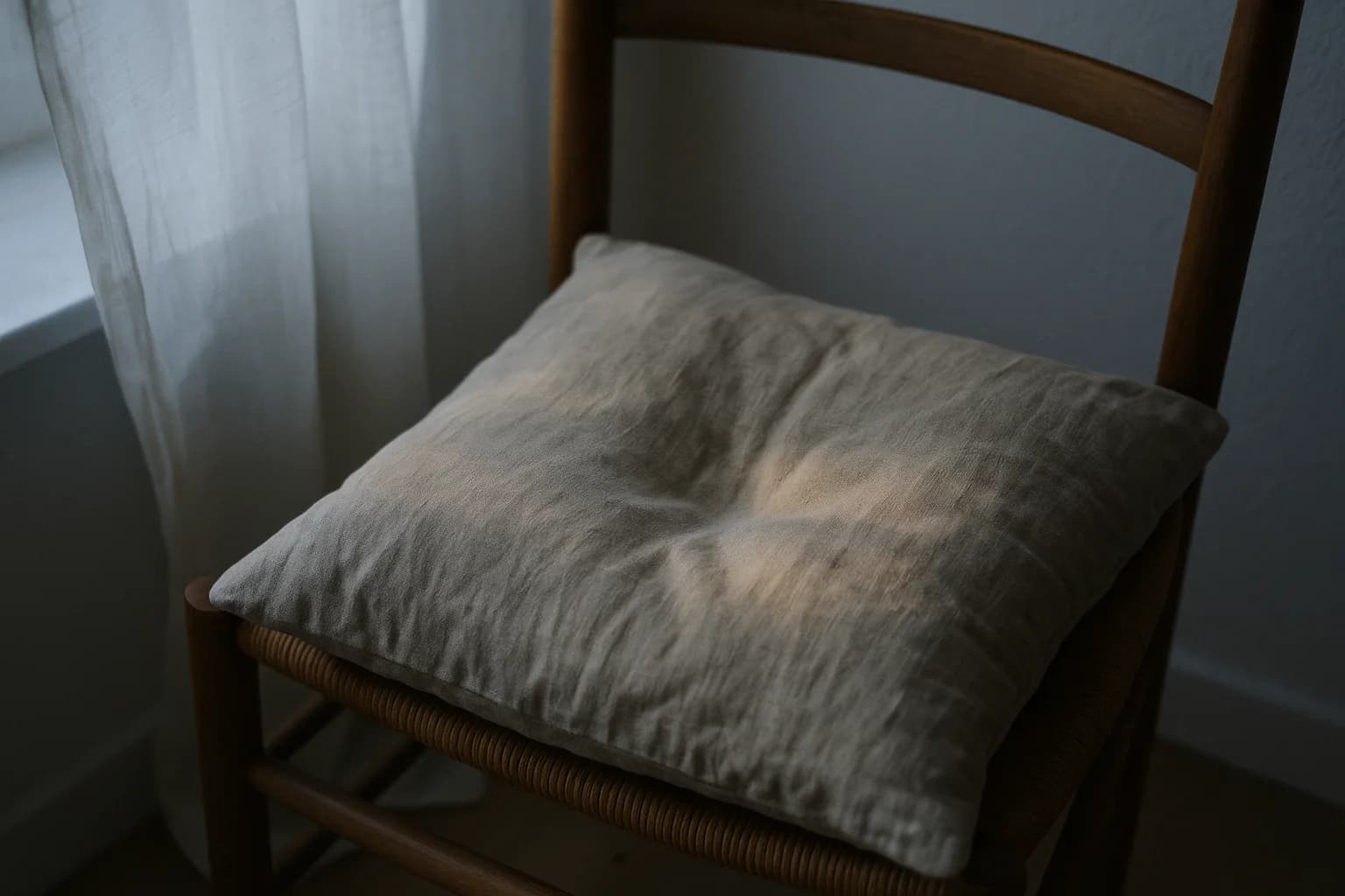Coussin de lin froissé sur une chaise en bois avec une légère empreinte en creux, lumière chaude de fin d'après-midi