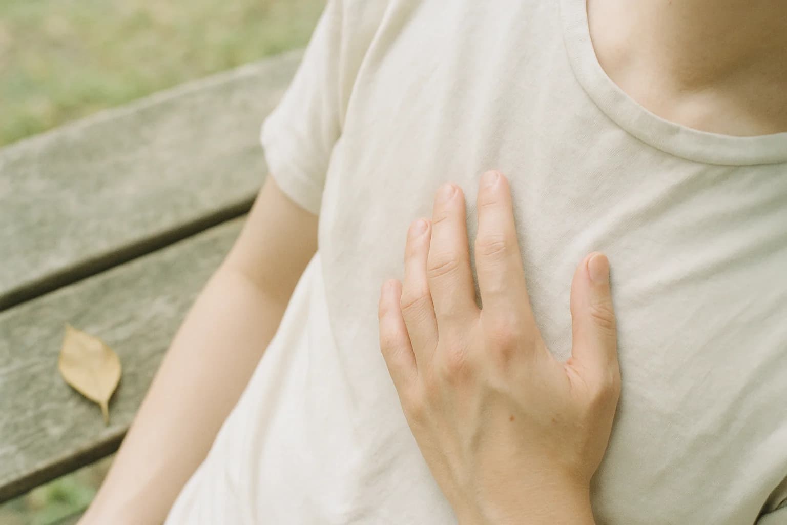 Une main posée à plat sur la poitrine, sur un tee-shirt de coton clair, geste d'auto-compassion et d'acceptation de soi