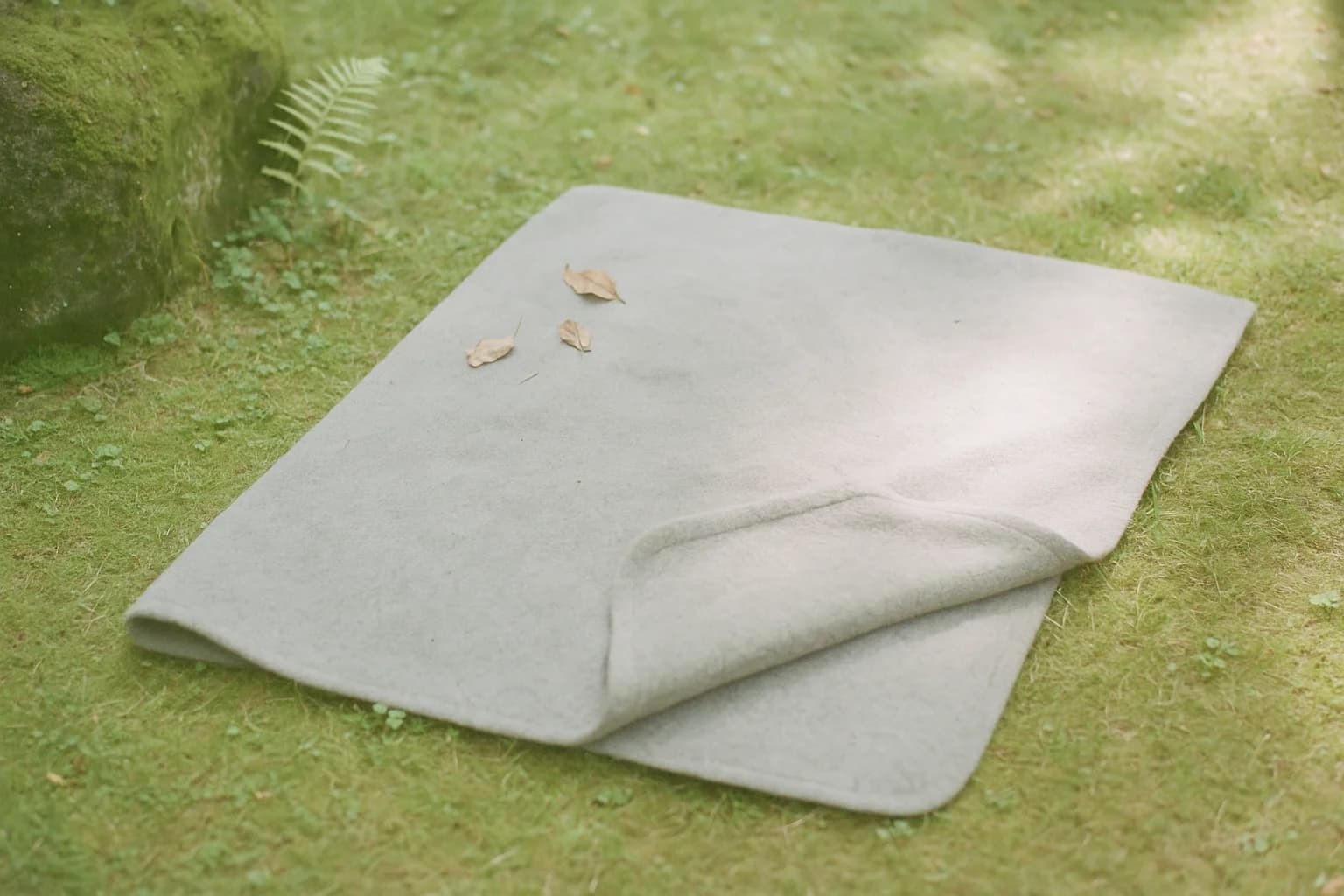 Une couverture de laine grise étalée à plat sur l’herbe courte d’un jardin, un coin replié