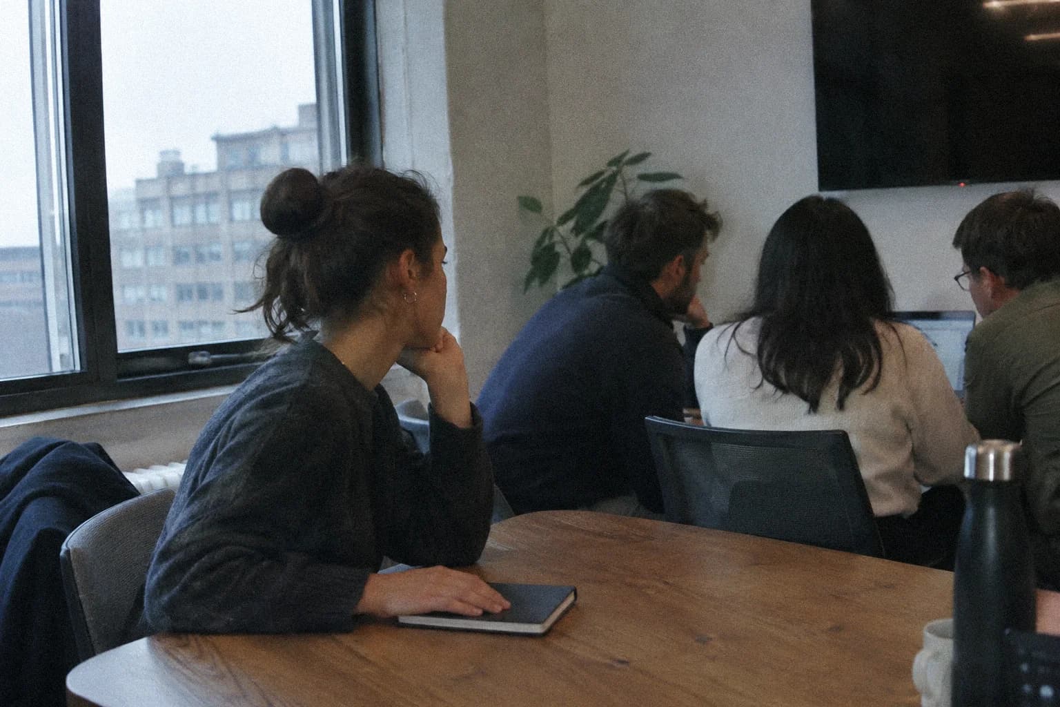 Peur du regard des autres : une femme assise à une table de réunion attend son tour de parler, la main sur un carnet fermé, pendant que ses collègues regardent tous un écran