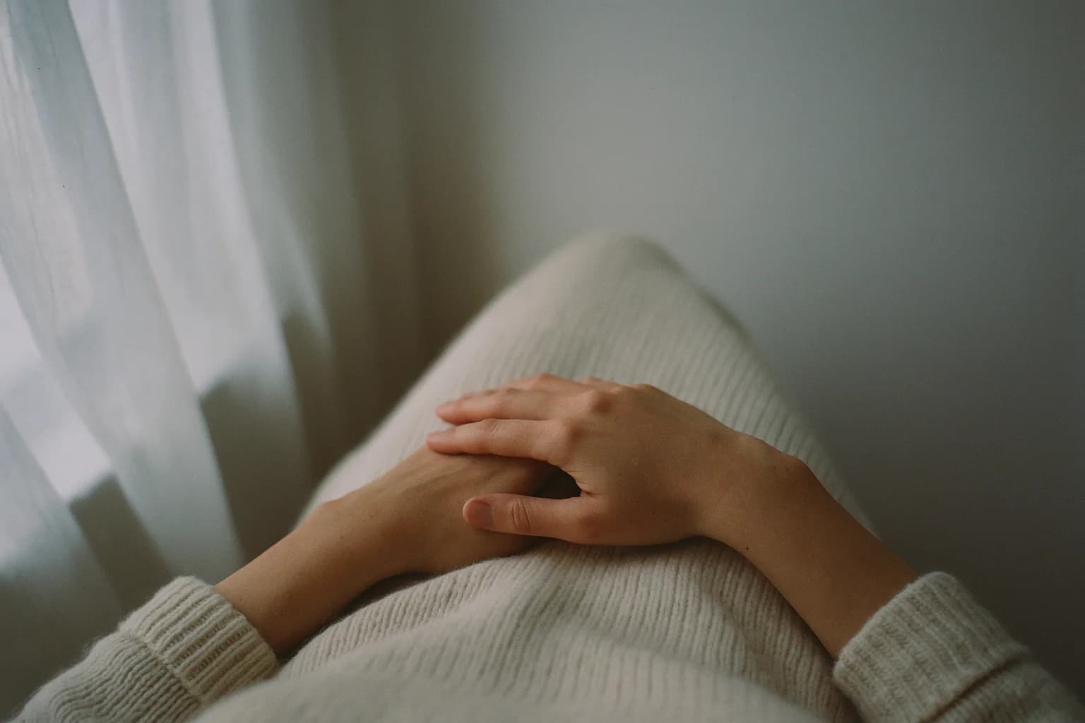 Deux mains croisées au repos sur un pull en maille crème, geste doux pour se réconcilier avec son corps